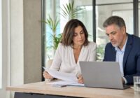 Attraktive realistische Berufstätige besprechen Altersteilzeit und Arbeitszeitplanung an einem Laptop in einem hellen Büro
