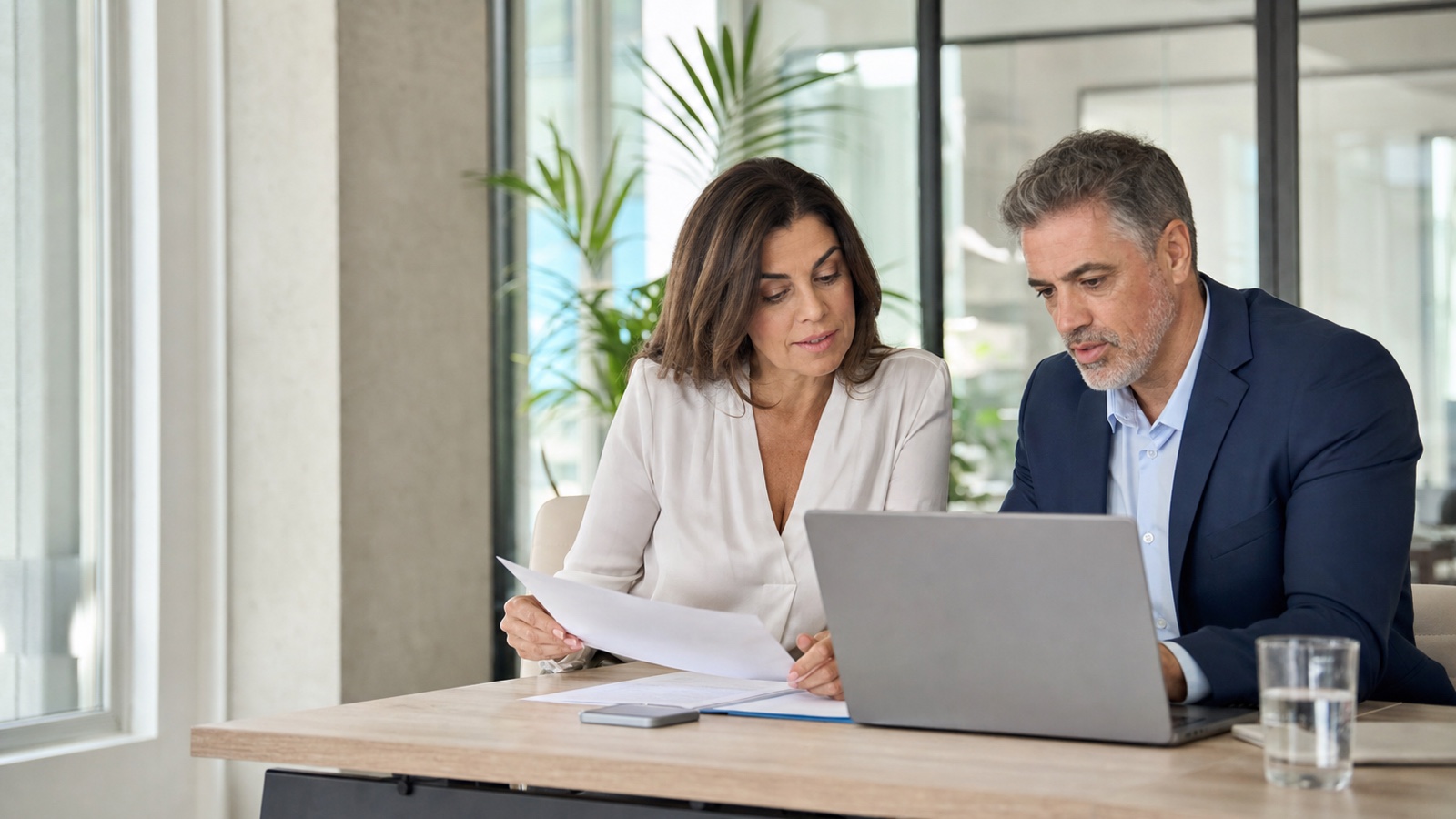 Attraktive realistische Berufstätige besprechen Altersteilzeit und Arbeitszeitplanung an einem Laptop in einem hellen Büro