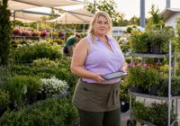 Blonde erwachsene Beschäftigte prüft in einem sommerlichen Gartencenter eine kurzfristige Dienstplanänderung