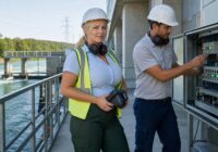 Blonde erwachsene Energietechnikerin prüft an einem sommerlichen österreichischen Wasserkraftwerk KI-gestützte Sensordaten