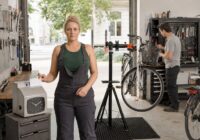 Blonde erwachsene Fahrradmechanikerin prüft in einer sommerlichen österreichischen Werkstatt ihr Arbeitszeitkonto