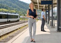 Blonde erwachsene Grenzgängerin mit Unterlagen an einem sommerlichen Bahnhof nahe der österreichischen Grenze
